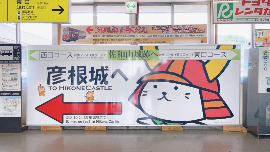 ひこにゃんが彦根城の方向を指し示す案内板（JR彦根駅改札前）